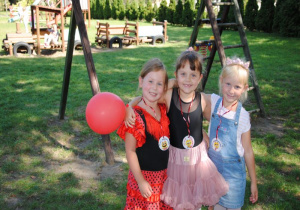 dziewczynki: cyganka, baletnica i księżniczka stoją w ogrodzie z czerwonym balonem obok huśtawki w ogrodzie